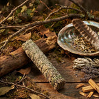 Bâton de fumigation sauge et palo santo, herbes beige vert ficelées de vert, posé sur bois avec coquille d’ormeau, plume et éclats de bois.