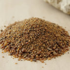 Gros plan sur un monticule de grains d'Encens Benjoin du Siam, montrant un mélange de poudre et de petits morceaux de résine brun-doré et ambré.