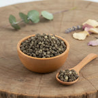 Grains de résine d'Encens Benjoin de Sumatra, de couleur gris-vert foncé, dans un petit bol en bois clair avec une cuillère, sur une tranche de tronc d'arbre rustique.