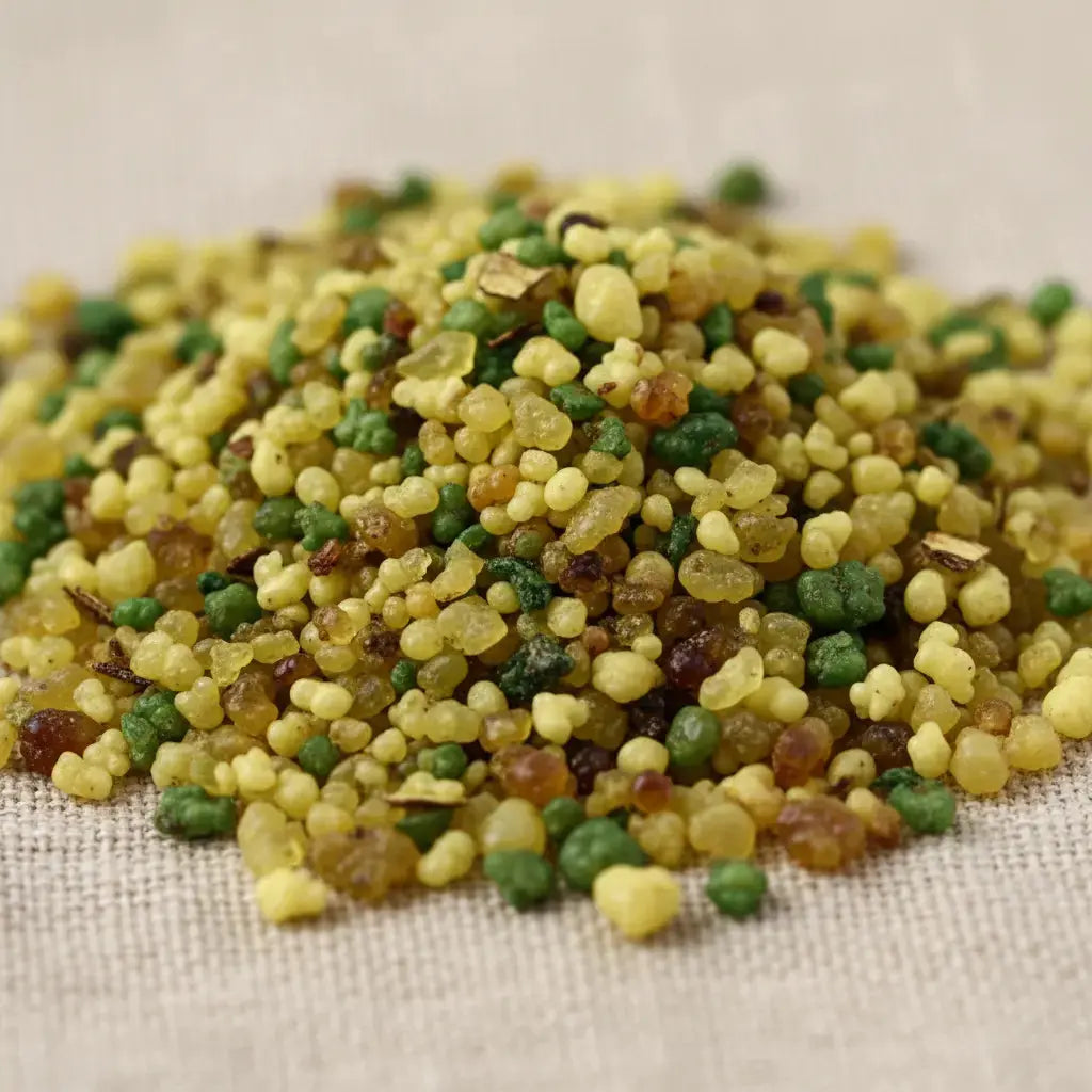 Gros plan sur un monticule de grains d'encens de résine Bergamote, montrant un mélange dense de jaune vif, de vert citron et de touches d'ambre, sur un fond en tissu clair.
