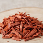 Bois de santal rouge pour fumigation, copeaux rouge-orangé en tas sur support en bois clair.