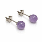 Une paire de boucles d'oreilles puces en argent, ornées de perles rondes en améthyste d'un violet tendre aux reflets naturels, présentées sur un fond blanc avec reflet.
