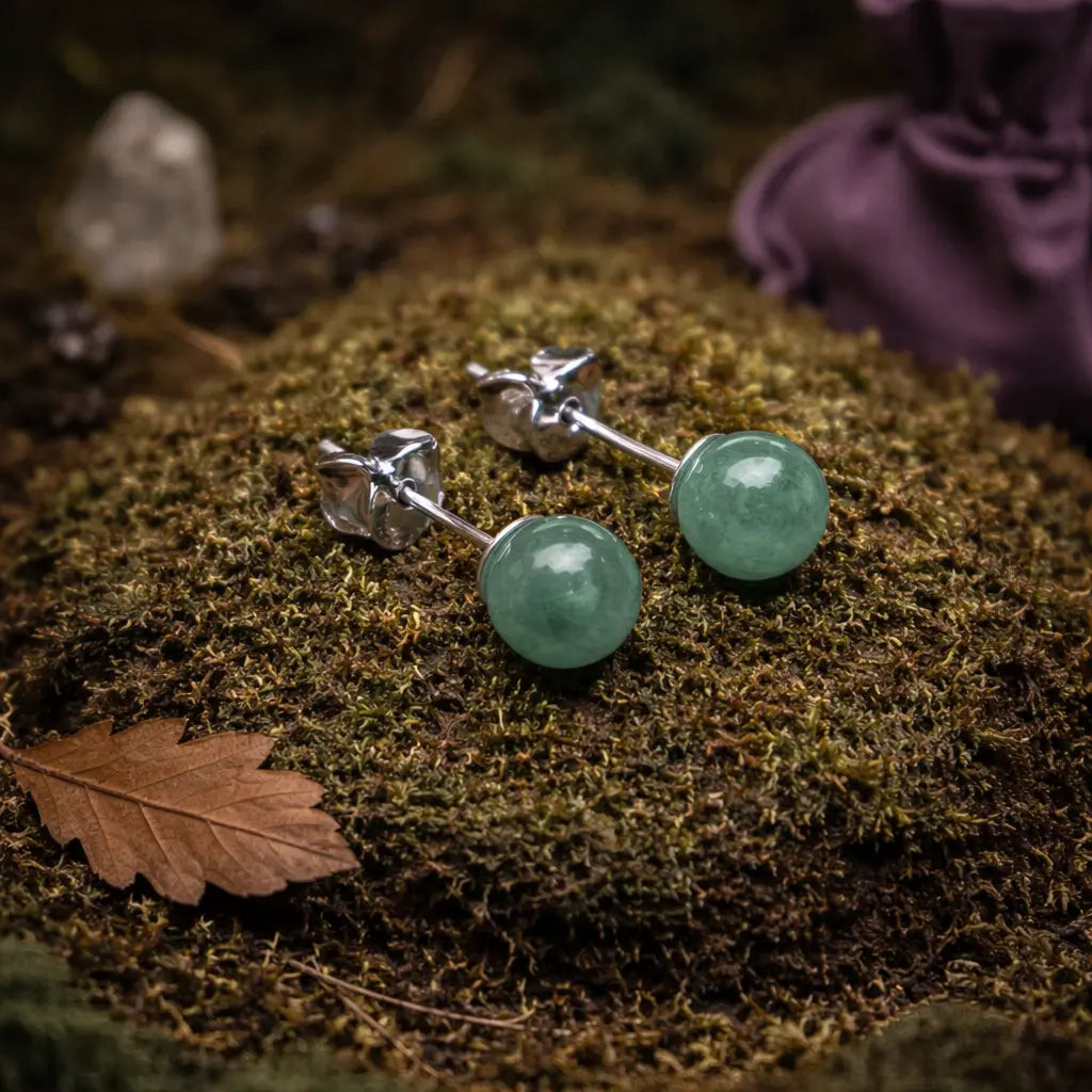 Paire de boucles d'oreilles clous en perles d'aventurine d'un vert tendre et herbacé, présentées sur un dôme de mousse forestière avec une feuille d'automne.