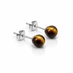 Une paire de boucles d'oreilles puces en argent, ornées de perles rondes en œil de tigre aux reflets chatoyants marron et dorés, présentées sur un fond blanc avec reflet.