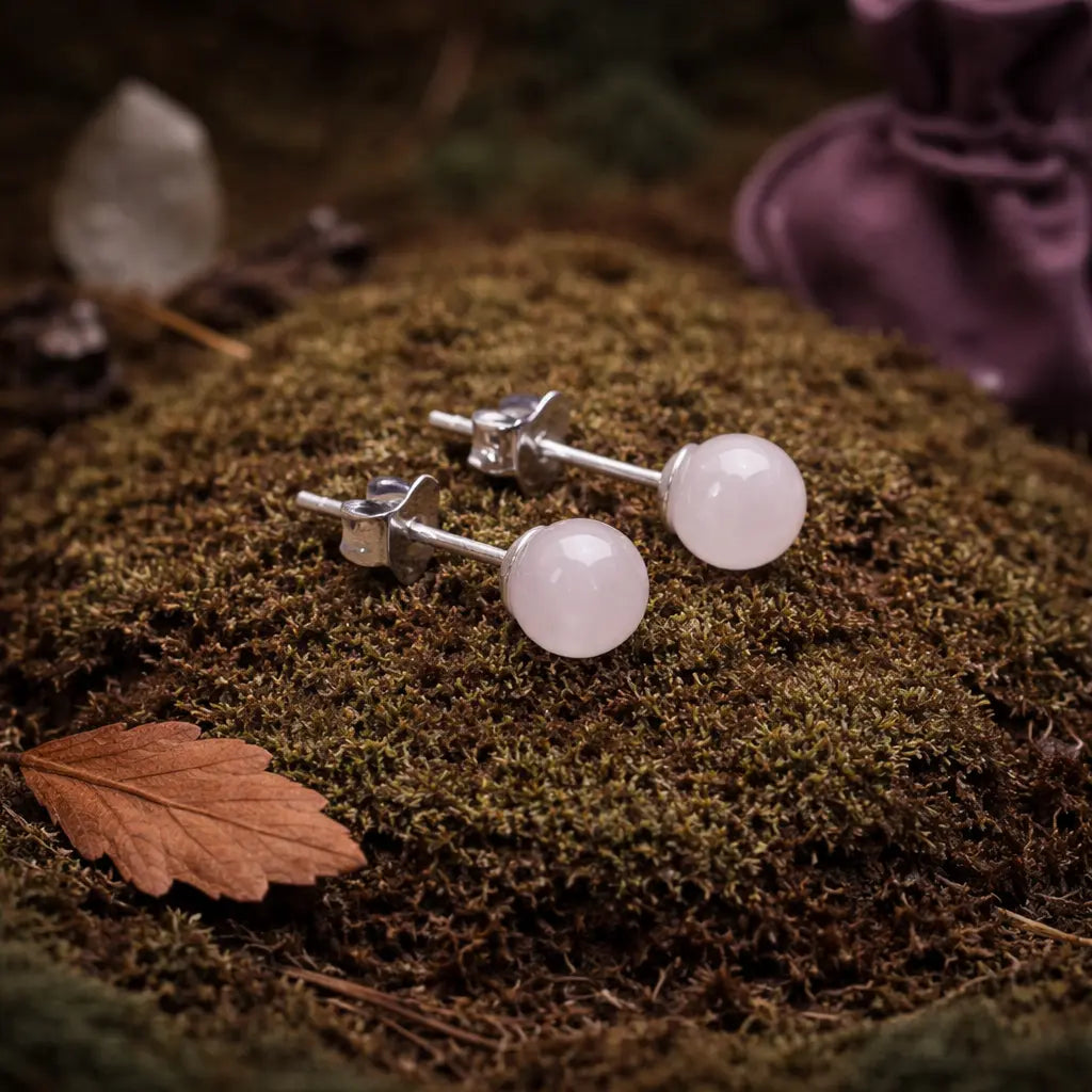 Paire de boucles d'oreilles clous ornées de perles de quartz rose poudré, délicatement posées sur une mousse forestière brune sous une lumière tamisée.