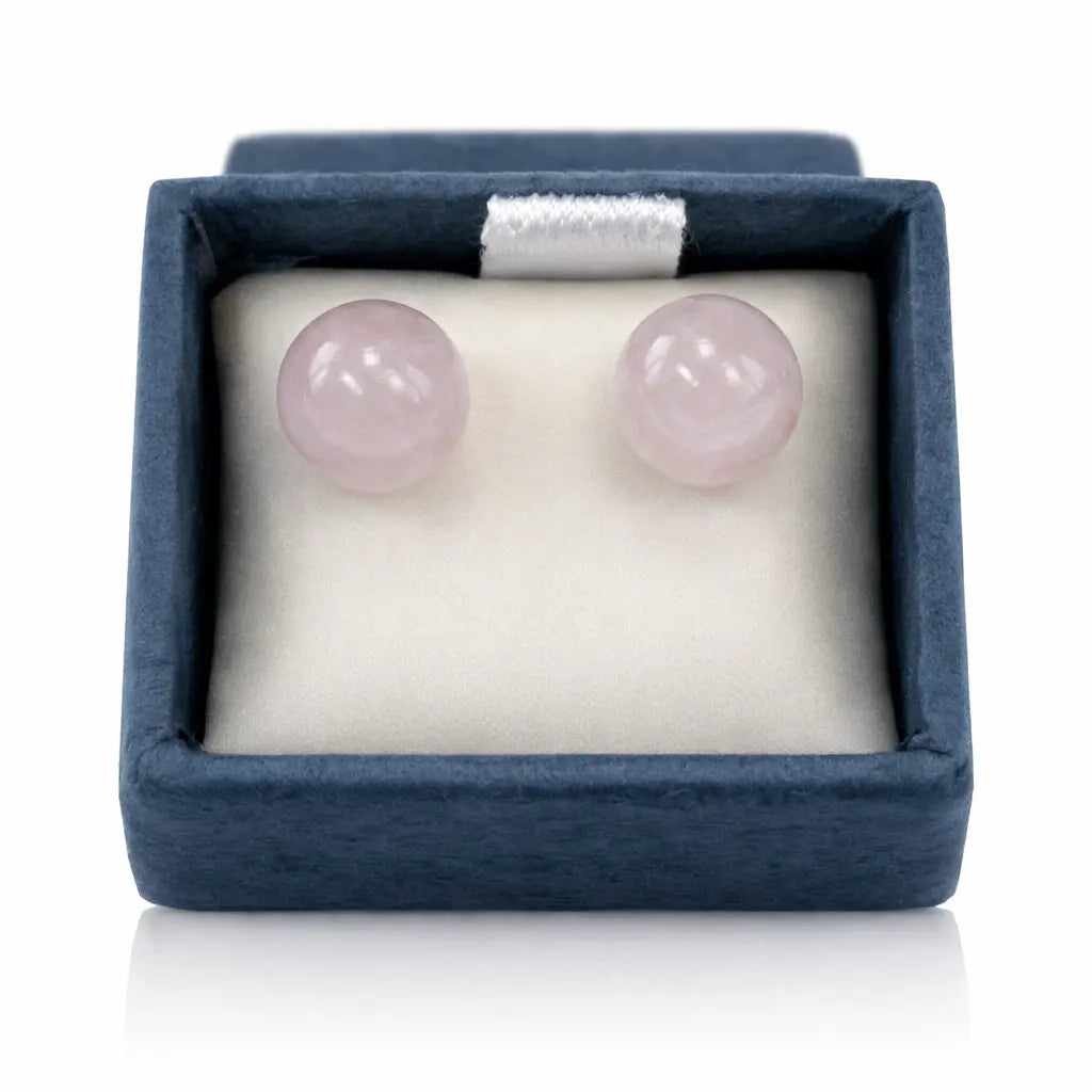Une paire de boucles d'oreilles puces en quartz rose, présentant deux perles rondes et polies délicatement disposées dans leur écrin bleu sur un coussinet blanc.