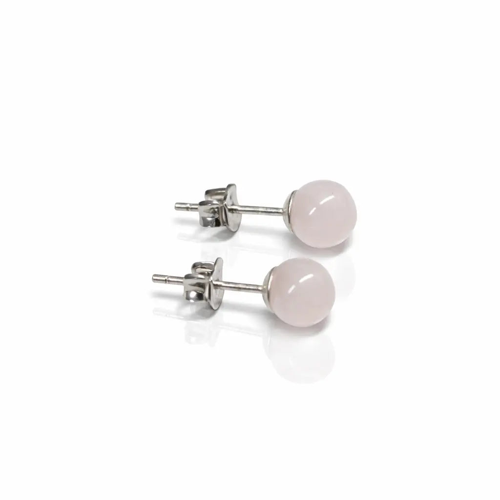 Une paire de boucles d'oreilles puces en argent, ornées de perles rondes et lisses en quartz rose pâle, présentées sur un fond blanc avec un reflet délicat.