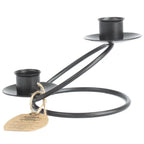 Un bougeoir double en fer forgé noir au design épuré, composé d'une base circulaire et de deux supports à bougies décalés en hauteur, présenté sur un fond blanc avec une étiquette artisanale.