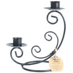 Un bougeoir double en fer forgé noir, caractérisé par ses volutes décoratives et ses deux coupelles réceptacles à des hauteurs différentes, présenté sur un fond blanc avec une étiquette artisanale.