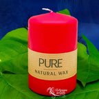 Bougie pilier rouge en cire naturelle « PURE », avec étiquette beige, posée sur des feuilles vertes (L’Echoppe de Gaïa).