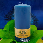 Bougie pilier bleu nuit en cire naturelle « PURE », avec étiquette beige, posée sur des feuilles vertes (L’Echoppe de Gaïa).