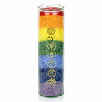 Une bougie pilier aux couleurs des 7 chakras dans un haut contenant cylindrique en verre, ornée des symboles sacrés dorés correspondants, présentée sur un fond blanc.