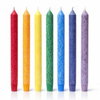 Un lot de sept bougies flambeaux aux couleurs des 7 chakras, présentant une texture cristallisée, disposées debout sur un fond blanc avec un léger reflet à leur base.