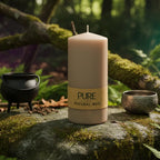 Bougie Cylindre Sable 40h Pure Candle avec bandeau papier naturel, posée sur un rocher moussu en forêt, accompagnée d'un chaudron et d'un bol chantant pour un rituel d'ancrage.