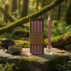 Boîte de 4 bougies longues rose antique Pure Candle posée sur un rocher moussu en forêt, accompagnée d'un petit chaudron et d'un bol chantant pour un rituel d'amour et de douceur.