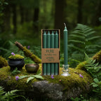 Boîte de 4 bougies longues vert émeraude Pure Candle posée sur un rocher moussu en forêt, accompagnée d'un petit chaudron et de fleurs violettes pour un rituel de magie verte.