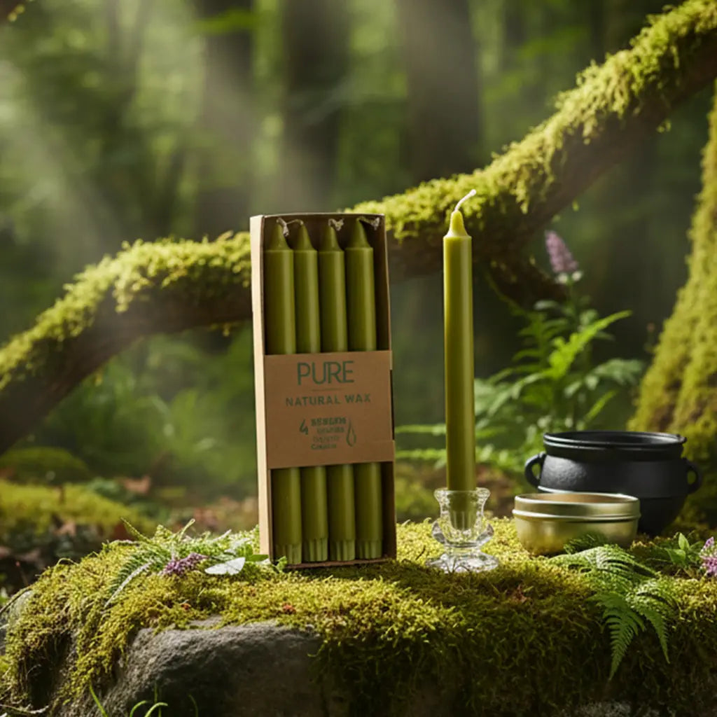 Boîte de 4 bougies longues vert olive Pure Candle dressée sur un rocher couvert de mousse en forêt, accompagnée d'un petit chaudron et d'accessoires de rituel naturel.
