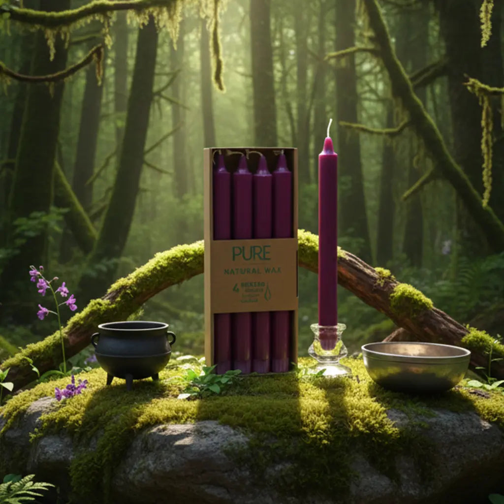 Boîte de 4 bougies longues violettes Pure Candle posée sur un rocher moussu en forêt, entourée de fleurs mauves, d'un chaudron et d'un bol chantant pour un rituel spirituel.