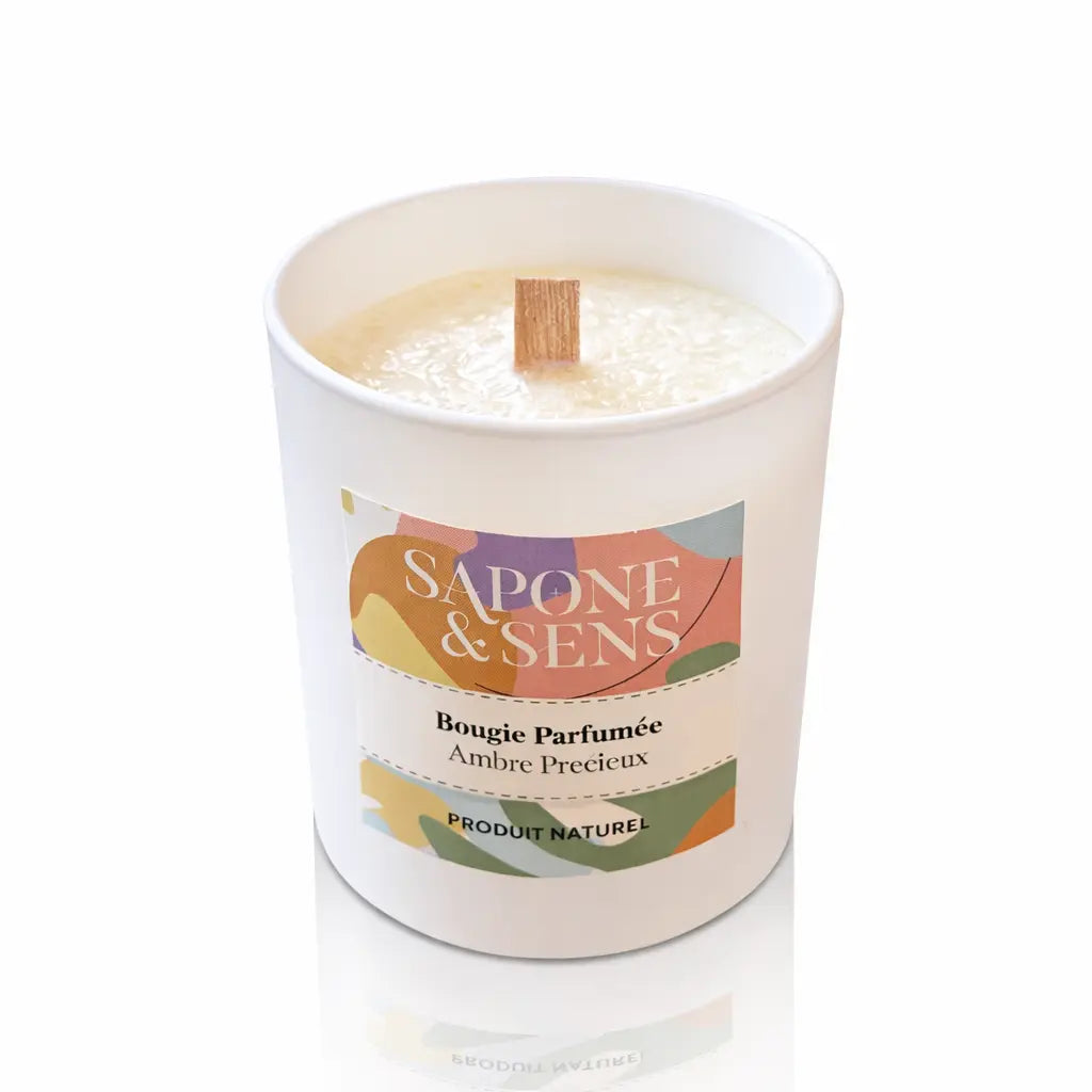 Une bougie parfumée naturelle « Ambre Précieux » de la marque Sapone & Sens, présentée dans un pot en céramique blanche avec une mèche en bois, sur un fond blanc.