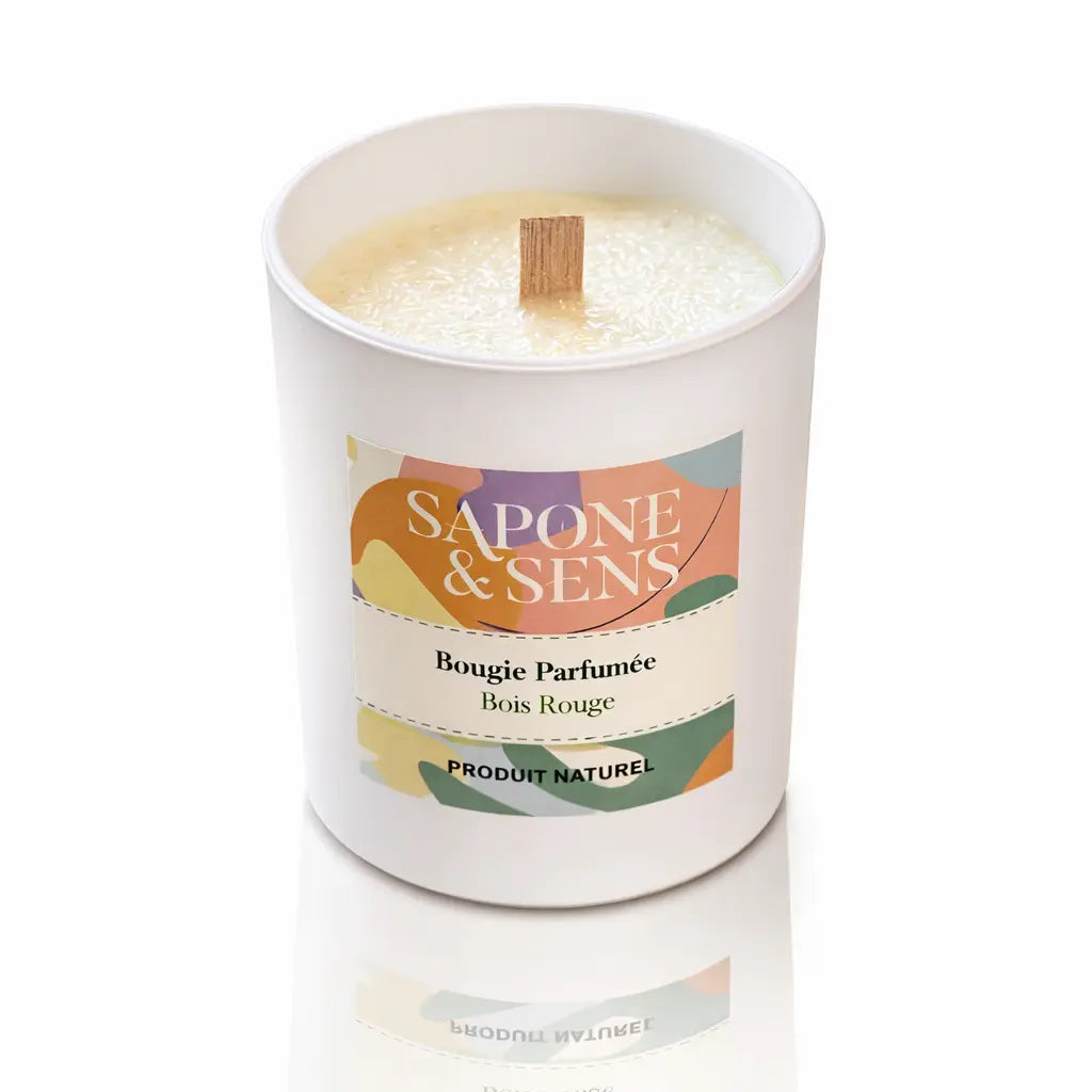Une bougie parfumée naturelle « Bois Rouge » de la marque Sapone & Sens, présentée dans un pot en céramique blanche avec une mèche en bois, sur un fond blanc.