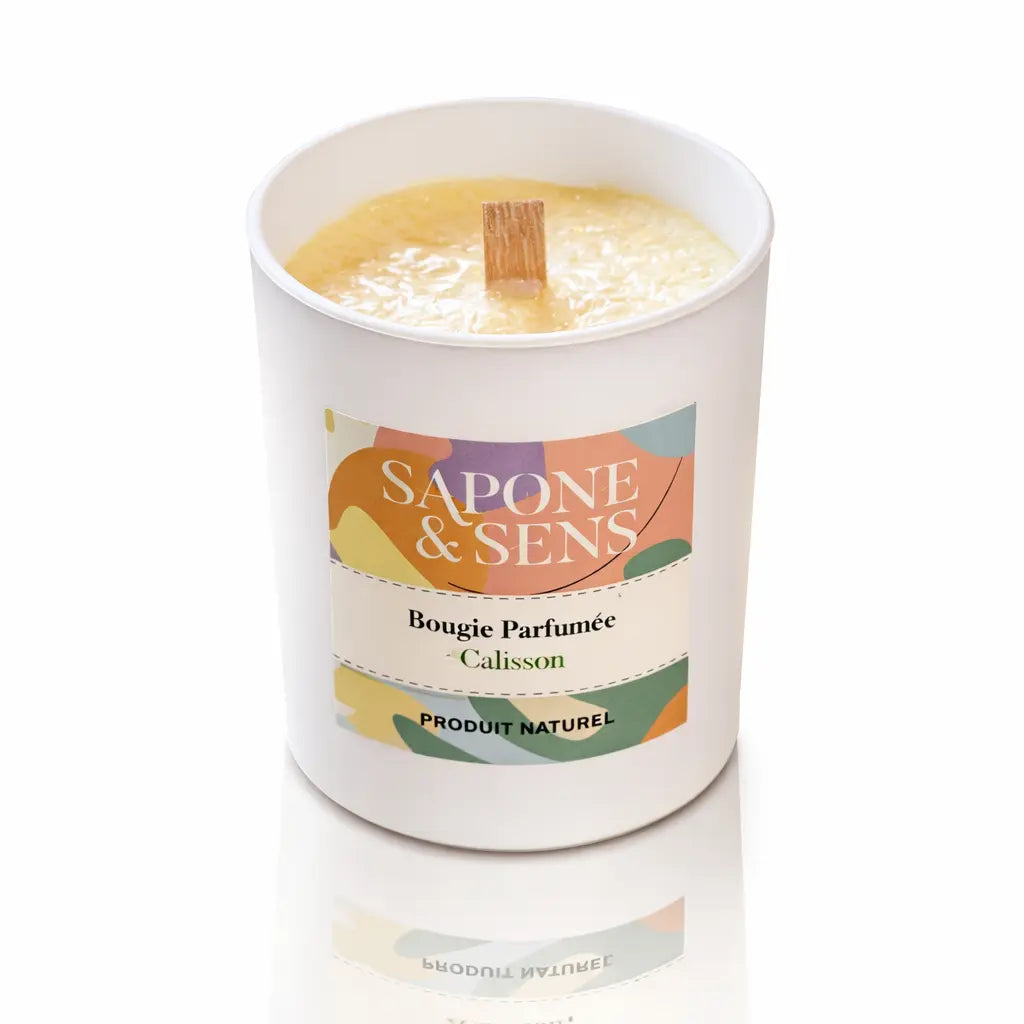 Une bougie parfumée naturelle « Calisson » de la marque Sapone & Sens, présentée dans un pot en céramique blanche avec une mèche en bois, sur un fond blanc.