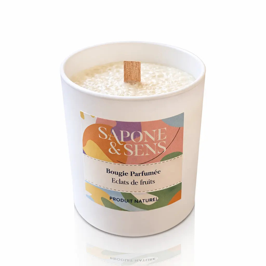 Une bougie parfumée naturelle « Éclats de fruits » de la marque Sapone & Sens, présentée dans un pot en céramique blanche avec une mèche en bois, sur un fond blanc.