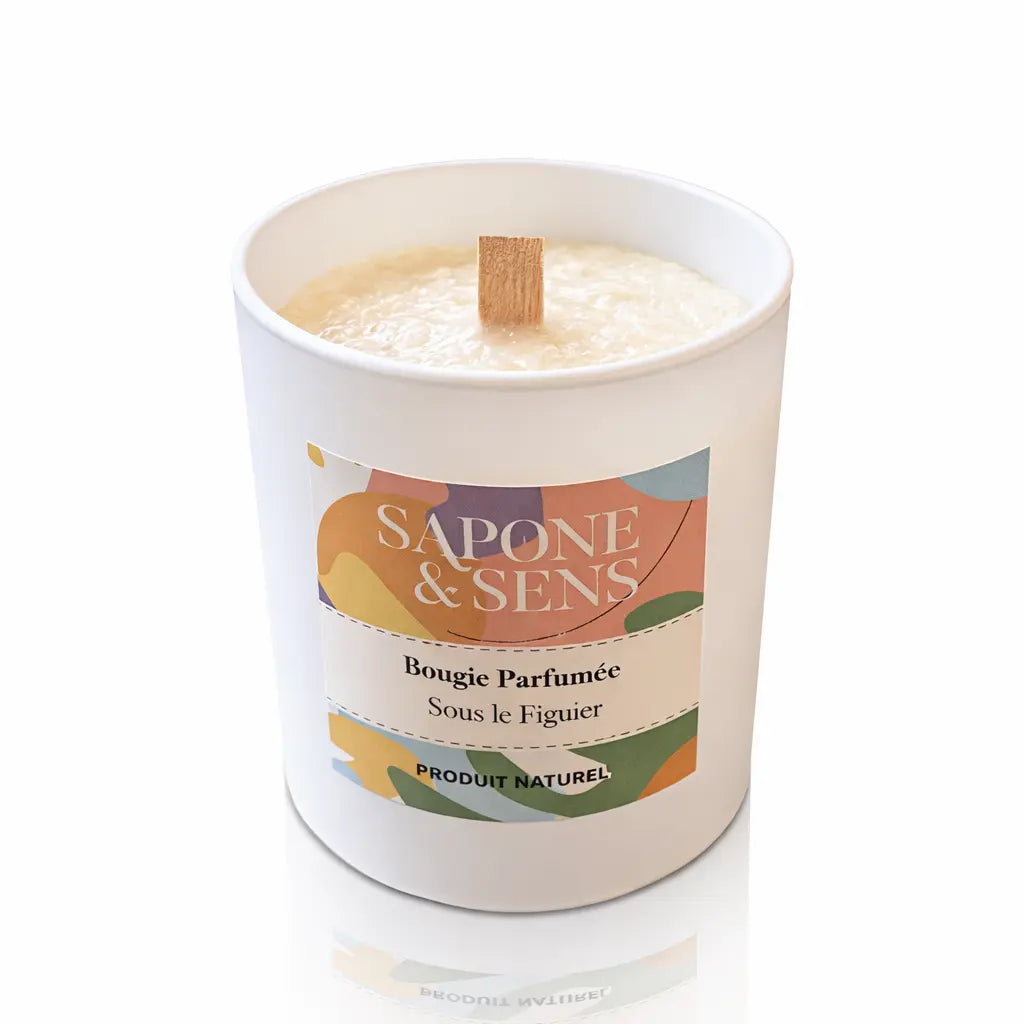 Une bougie parfumée naturelle « Sous le Figuier » de la marque Sapone & Sens, présentée dans un pot en céramique blanche avec une mèche en bois, sur un fond blanc.