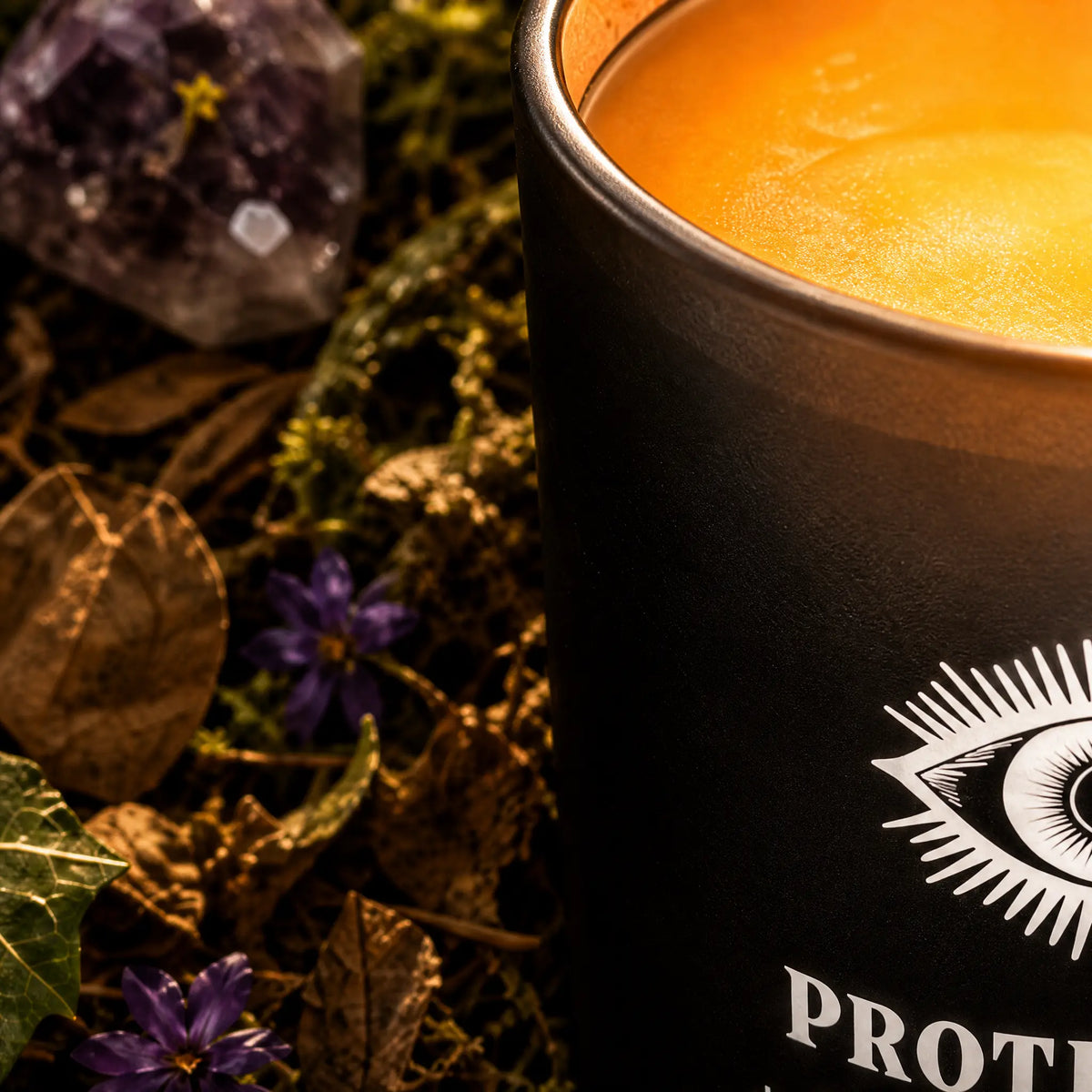 Gros plan sur la cire chaude d'une bougie Protection Spell Candle dans un pot noir illustré d'un œil, posée près d'un cristal d'améthyste et de petites fleurs violettes.   