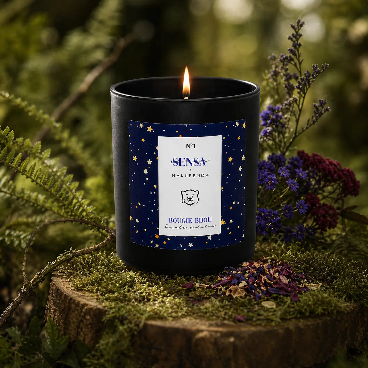 Texte Alt Image : Bougie parfumée Eskalia Escale Polaire à l'étiquette étoilée, allumée sur un socle de bois moussue, entourée de fleurs séchées violettes et de fougères dans un sous-bois.