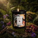 Bougie "Escale Zanzibar" Eskalia avec une étiquette aux tons orangés, posée sur un socle de bois naturel au milieu de plantes de sous-bois et de fleurs printanières.