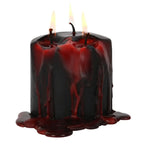 Une bougie pilier noire basse à trois mèches allumée, dont la cire rouge sang coule abondamment sur les parois et s'accumule à sa base, présentée sur un fond blanc.