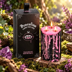 Bougie Antique Vampire Draculina 3 Mèches allumée aux coulures roses à côté de sa boîte, posée en forêt sur de la mousse.