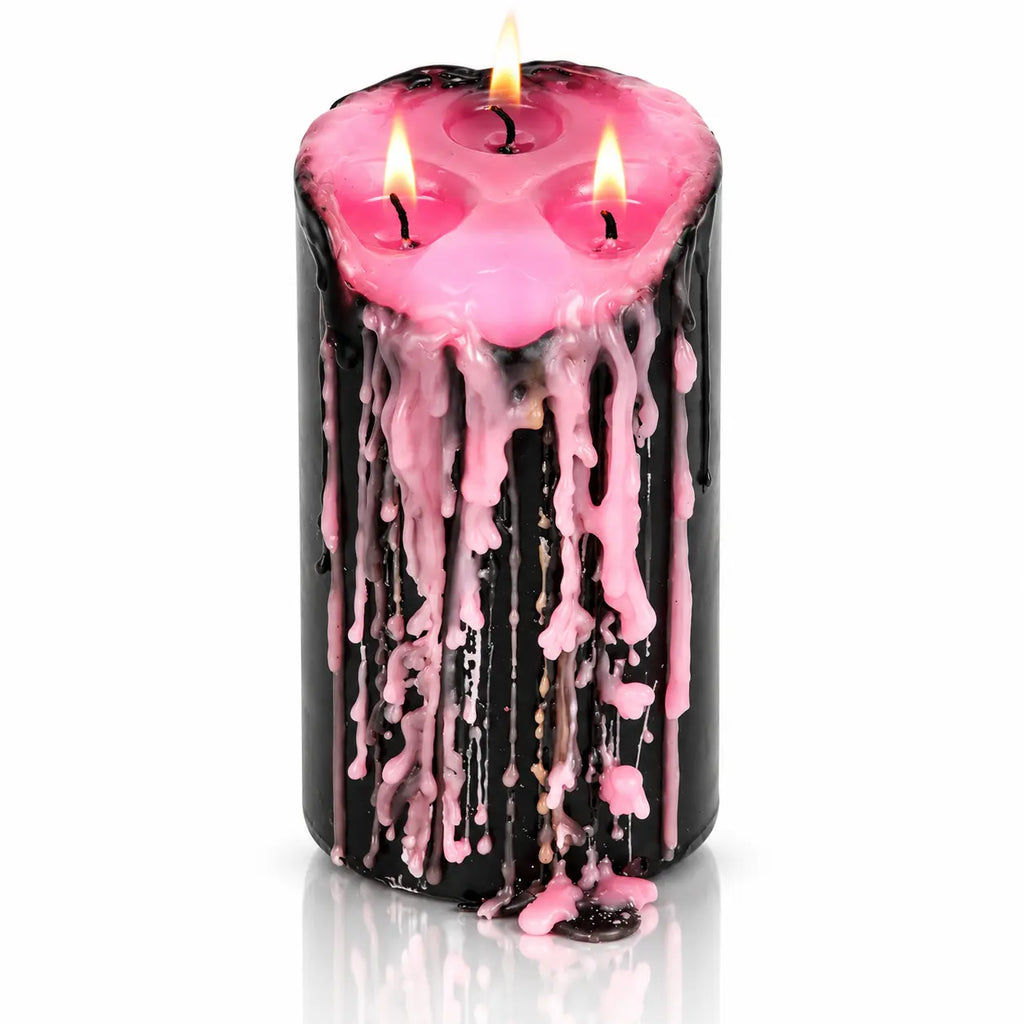 Grande bougie pilier vampire Draculina noire à 3 mèches allumées, laissant couler de la cire rose le long de ses parois, sur fond blanc avec reflet.