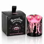 Bougie Antique Vampire Draculina 3 Mèches allumée à la cire rose à côté de sa boîte noire sur fond blanc.   