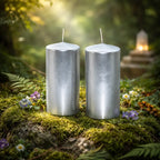 Duo de bougies piliers métalisées cylindre argent 100h de 20 cm de haut posées sur de la mousse naturelle en forêt.