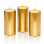 Un lot de trois bougies piliers métallisées dorées, de forme cylindrique, présentées debout sur un fond blanc avec un léger reflet à leur base.