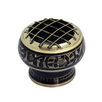 Brûle-encens en métal noir et doré avec grille supérieure croisée et motifs gravés sur la bague, posé sur fond blanc.