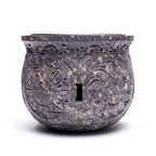 Brûle-encens en pierre stéatite sombre effet marbré, forme ronde décorée de fleurs sculptées, fente ajourée au centre, fond blanc.