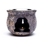 Brûle-encens en pierre stéatite sombre effet marbré, décor floral sculpté, cavité centrale avec chauffe-plat allumé, fond blanc.