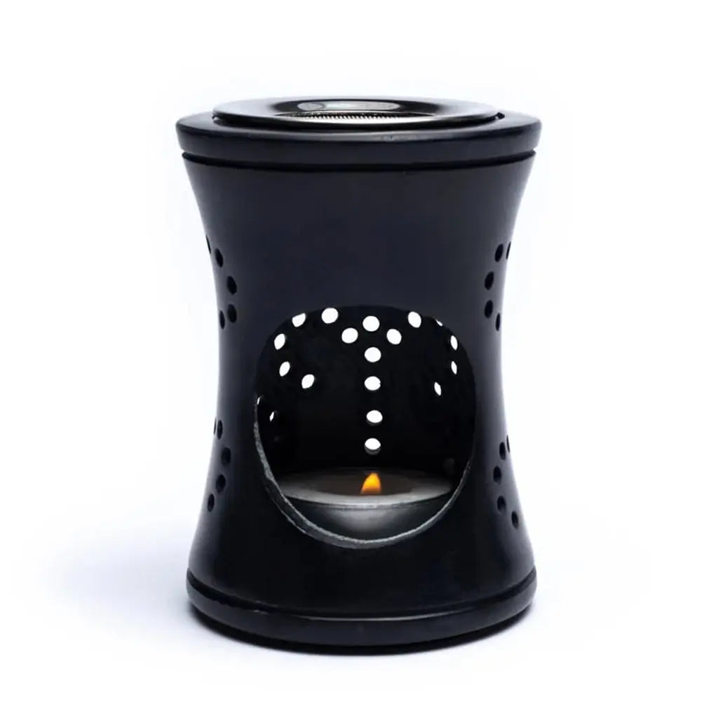 Brûle-encens en stéatite noire, forme cylindrique ajourée avec grande ouverture frontale laissant voir une bougie chauffe-plat allumée.
