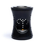 Brûle-encens en stéatite noire, forme cylindrique ajourée avec grande ouverture frontale laissant voir une bougie chauffe-plat allumée.