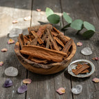 Coupelle en bois remplie de bâtons de cannelle bruns sur table en bois avec cristaux, pétales et petite coupelle en nacre.