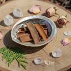 Coupelle en nacre remplie de bâtons de cannelle bruns sur rondin de bois décoré de cristaux et roses séchées.