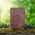 Carnet Ceinturé en Cuir Artisanal - Oeil de Tigre fermé par deux lanières, orné d'une pierre centrale, posé sur une branche moussue avec des fleurs violettes dans une forêt.
