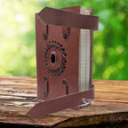 Un carnet en cuir artisanal marron doté de deux lanières de fermeture, orné en son centre d'une pierre d'onyx noire sertie dans une tresse de cuir, présenté sur un support en bois.