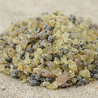 Gros plan sur des grains de résine d’encens Cathédrale jaunes, gris et bruns sur fond sableux.