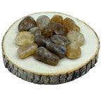 Un groupe de pierres de citrine naturelle roulées de qualité A, aux nuances fumées et miel translucides, disposé sur une rondelle de bois naturel.