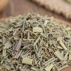 Brins de citronnelle séchée vert pâle coupés en petits morceaux en vrac sur support en bois.
