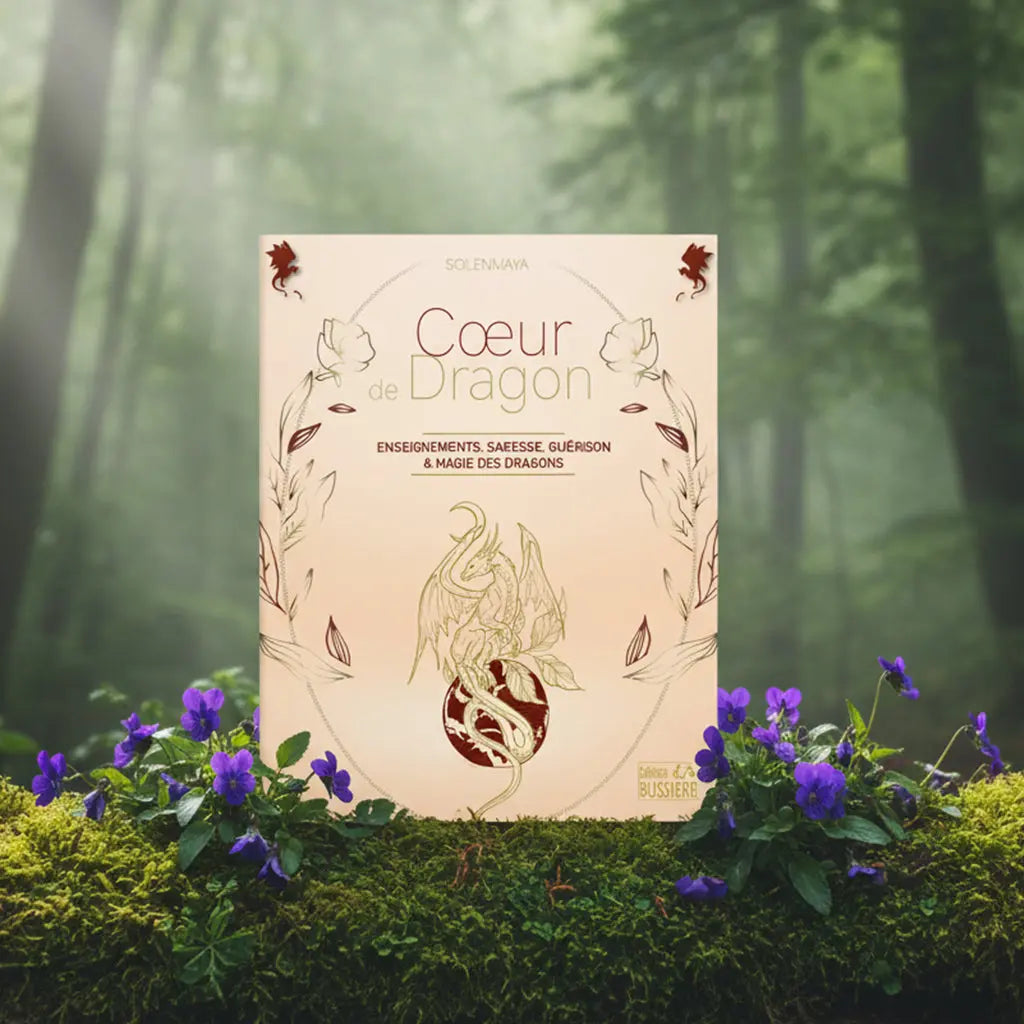 Livre Coeur de Dragon de Solenmaya posé verticalement sur de la mousse verte dans une forêt brumeuse, entouré de grappes de fleurs sauvages violettes.