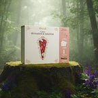 Coffret blanc Omsaé "Divination et Intuition" présenté sur une souche de bois moussue en pleine forêt, entouré de fleurs violettes et d'une lumière naturelle mystique.